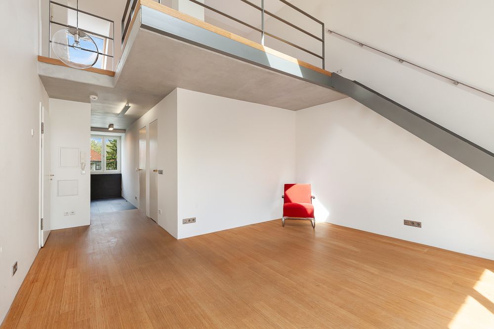 Heller Wohnraum mit Holzboden, rotem Stuhl und offener Galerie mit Metalltreppe.