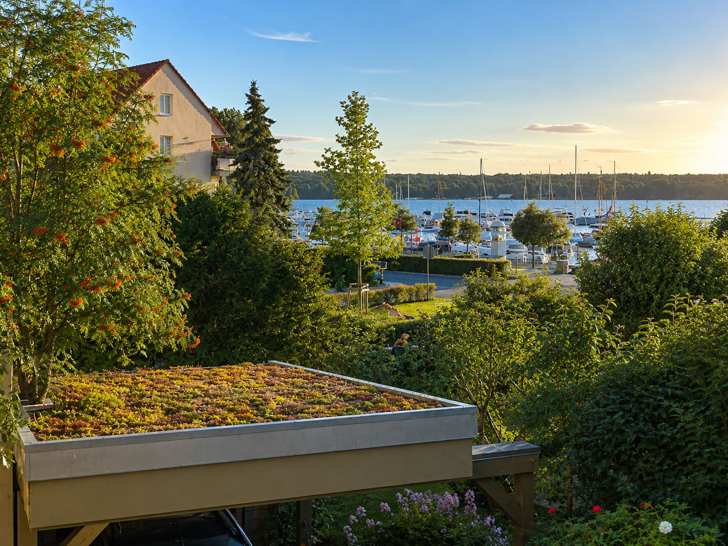 Begrüntes Carport-Dach vor Garten, im Hintergrund ein See mit Segelbooten bei Sonnenuntergang.