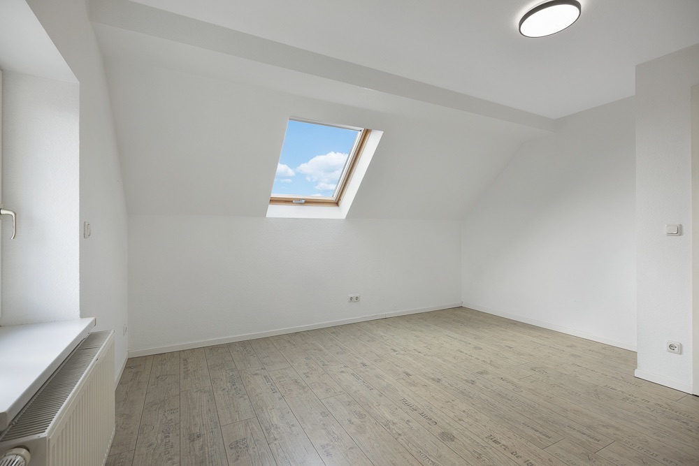 Leerer Raum mit Holzfußboden und Dachfenster, weiße Wände und Decke.