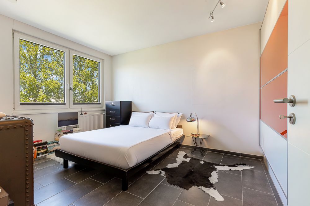 Helles Schlafzimmer mit Doppelbett, großem Fenster, Teppich und Kleiderschrank.