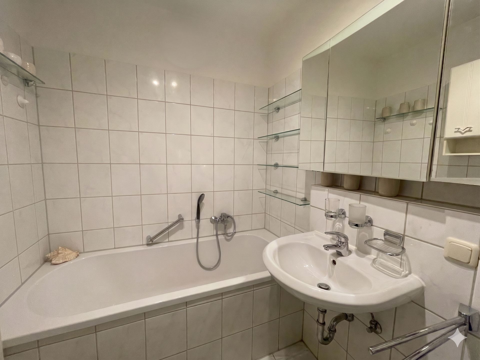Helles Badezimmer mit Badewanne, weißem Waschbecken und Spiegelschrank.