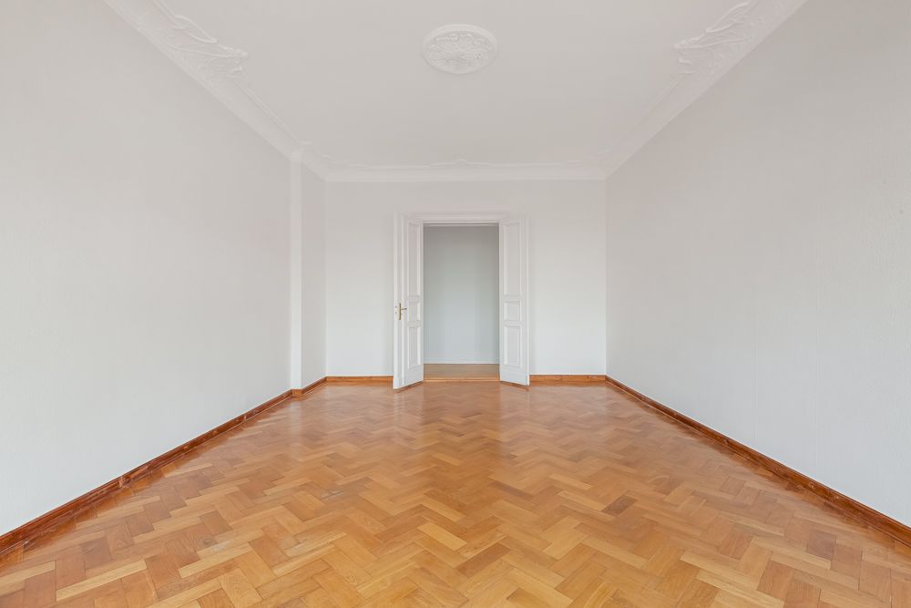 Leerer Raum mit Parkettboden, weißen Wänden und offener Doppeltür.