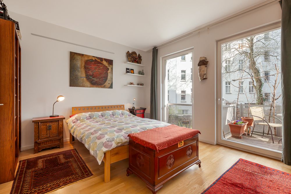 Helles Schlafzimmer mit Doppelbett, Holzmöbeln und Zugang zu einem Balkon mit Stühlen und Pflanzen.