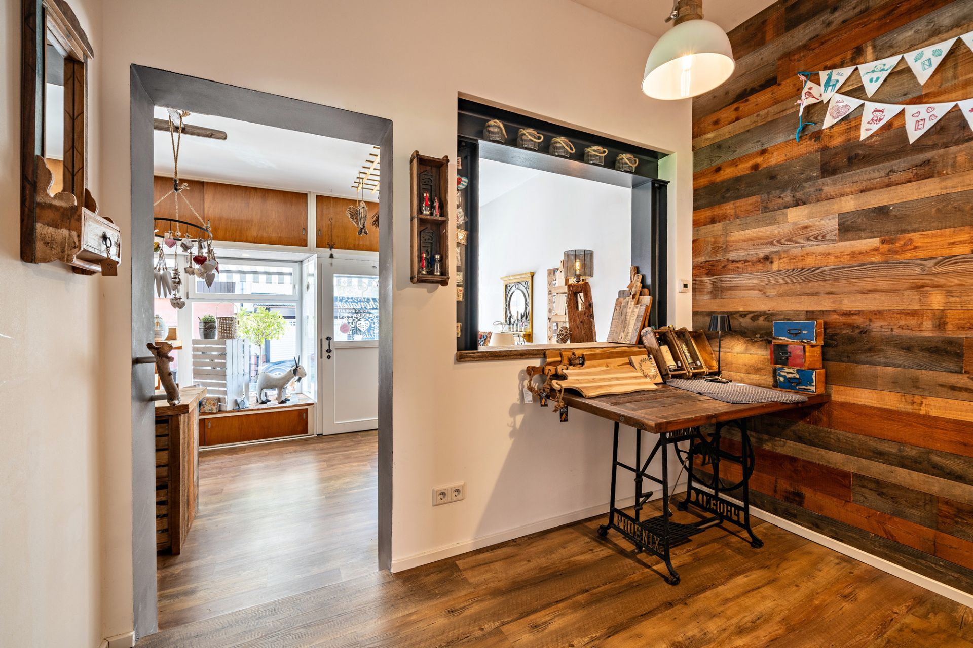 Heller Flur mit Holzwand, Dekotisch und Durchgang zu einem Wohnraum mit großen Fenstern.