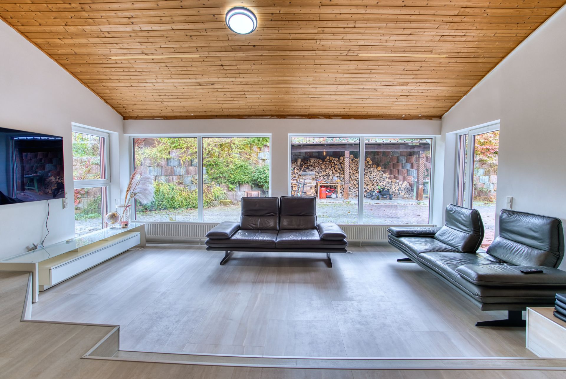 Modernes Wohnzimmer mit zwei schwarzen Sofas, großen Fenstern und Holzdecke.