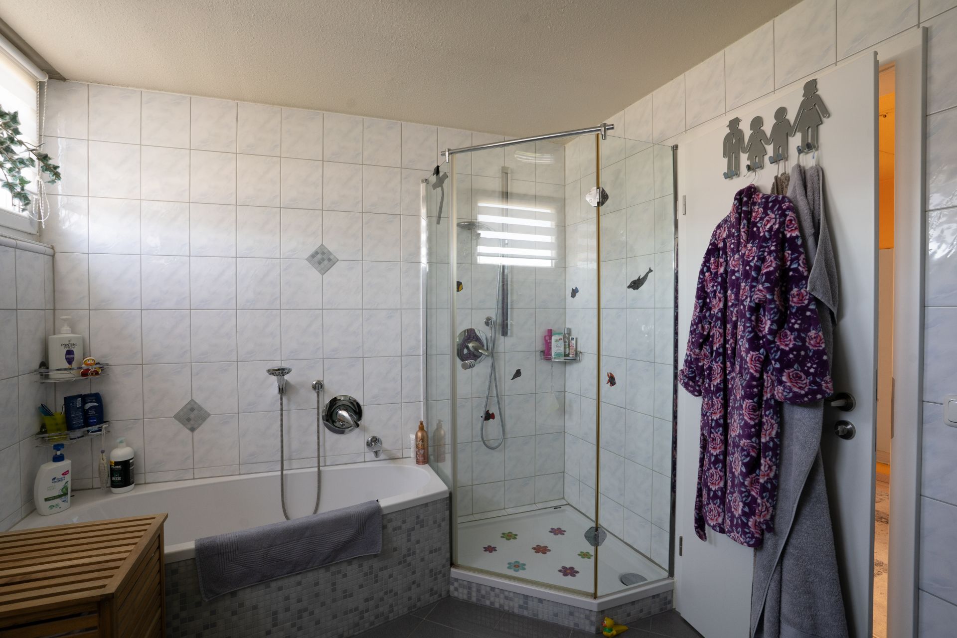 Gefliestes Badezimmer mit Badewanne, Eckdusche und einem lila Bademantel an der Tür.