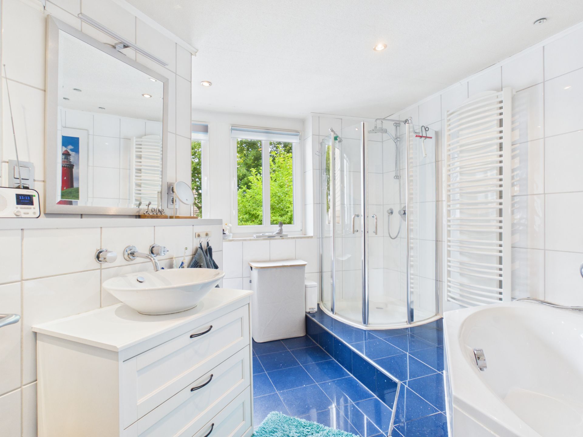 Modernes Badezimmer mit Dusche, Badewanne, Waschbecken und Fenster, blaue Fliesen am Boden.