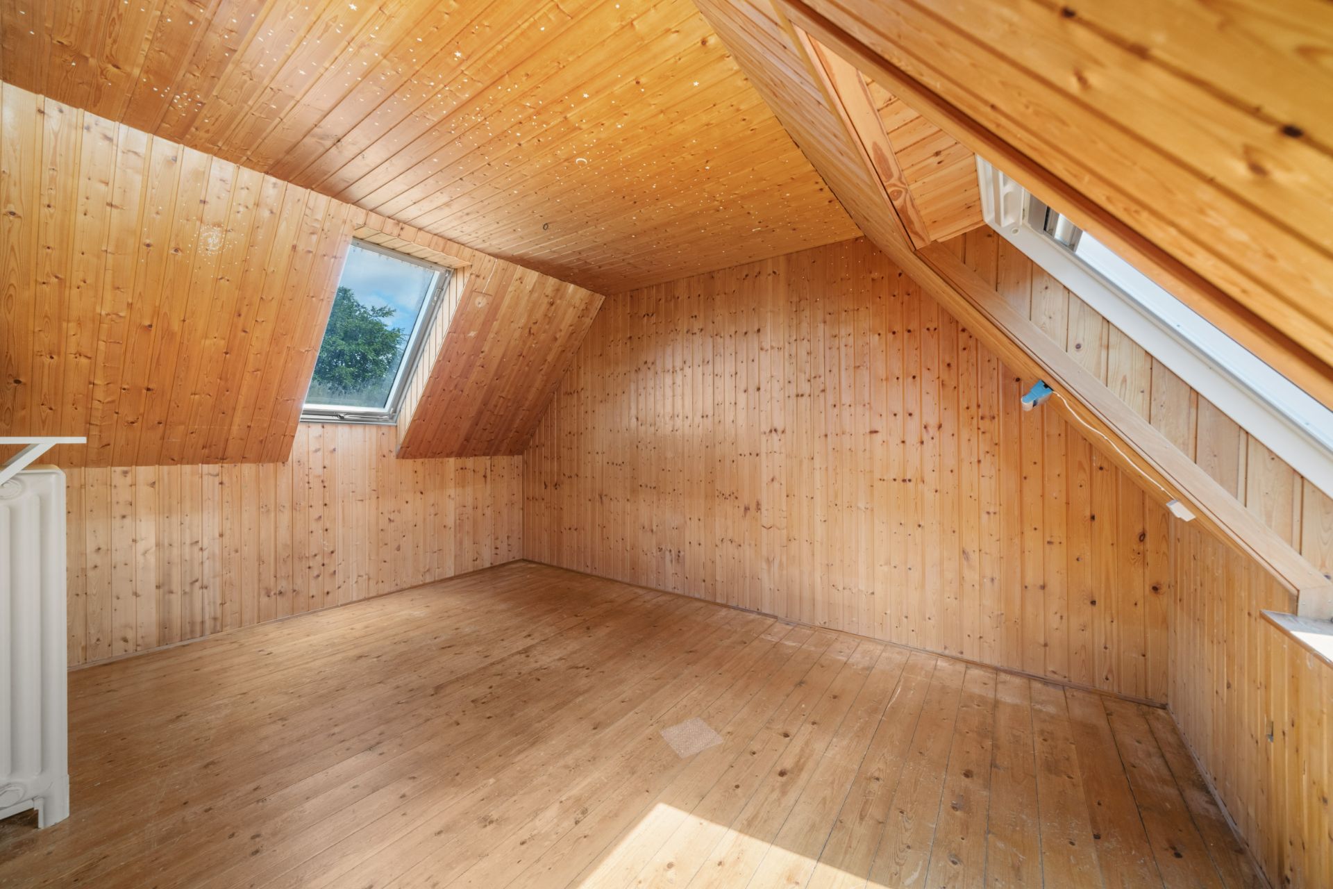 Zimmer mit Holzverkleidung und zwei Dachfenstern, viel Tageslicht.