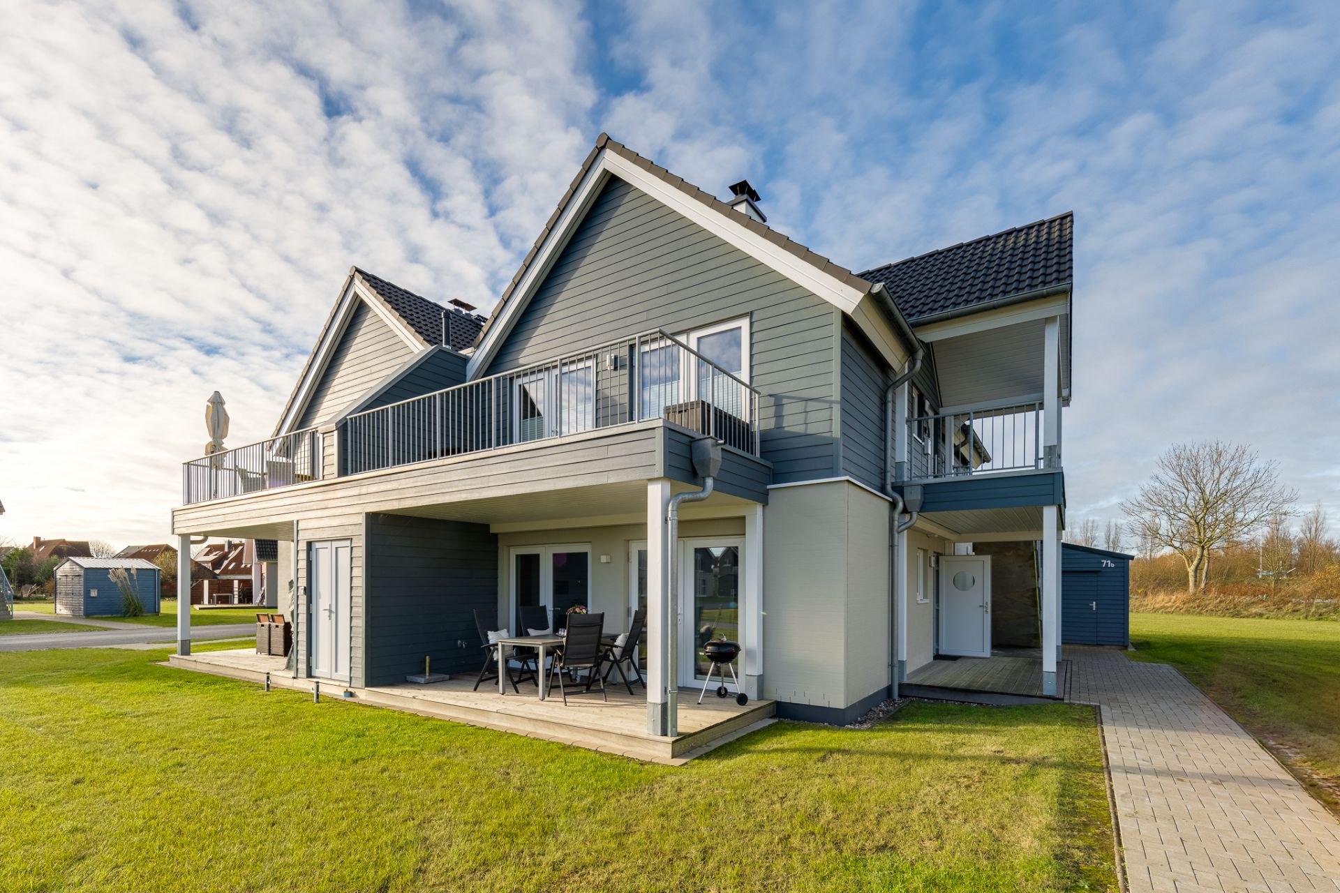 Modernes zweistöckiges Haus mit Terrasse, Balkon und Garten bei Tageslicht.
