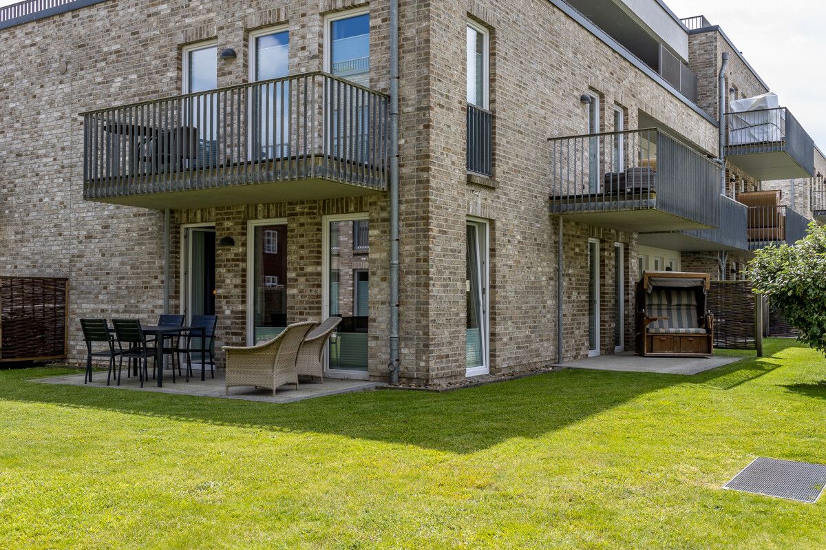 Erdgeschosswohnung mit Terrasse, Gartenmöbeln, Strandkorb und Balkon in moderner Backsteinfassade.