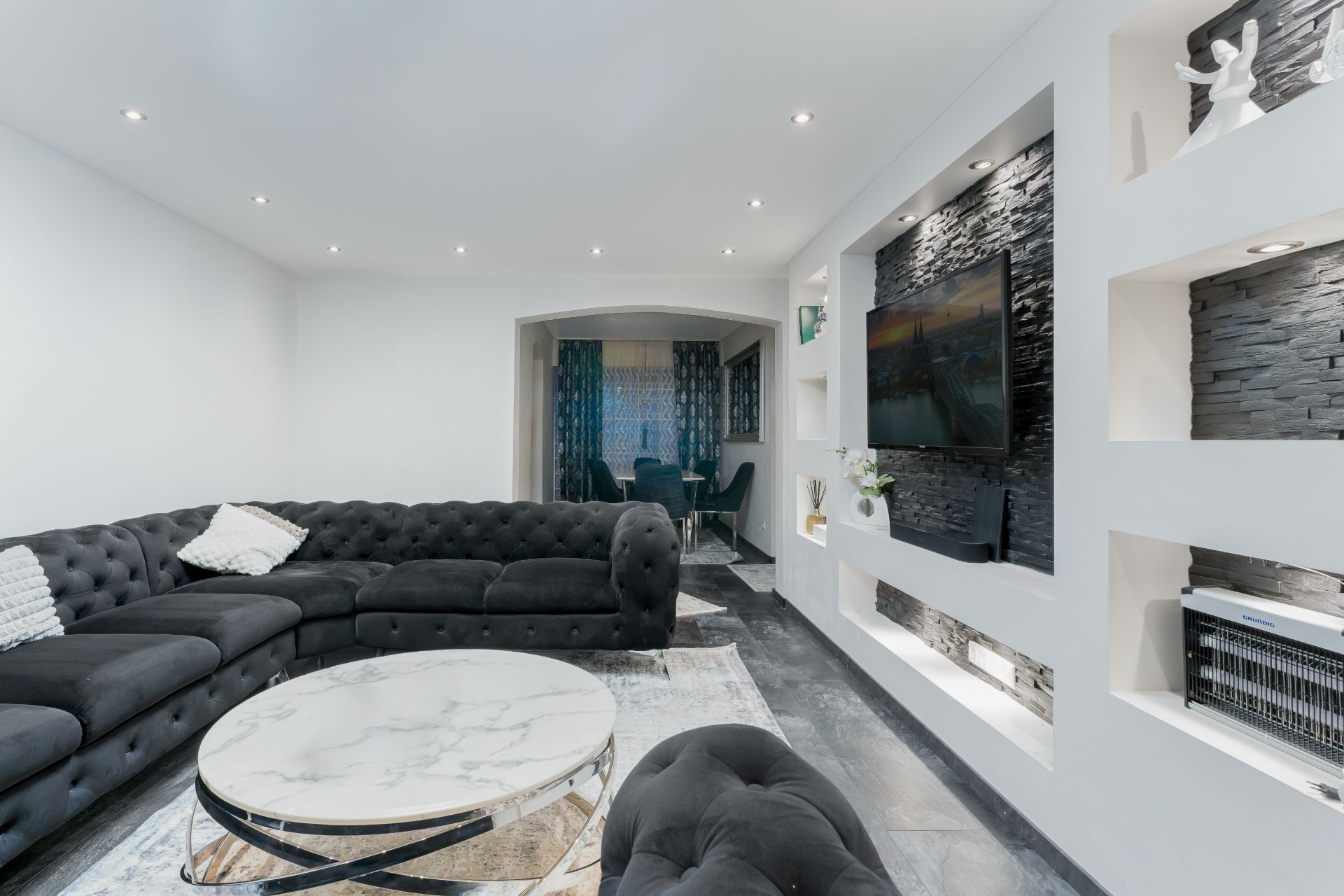 Modernes Wohnzimmer mit schwarzem Sofa, rundem Couchtisch und Wand mit Fernseher.