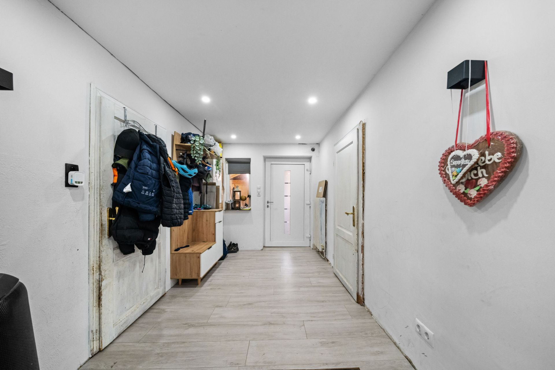 Flur mit Garderobe, Jacken, Türen und einem Herzanhänger an der Wand.