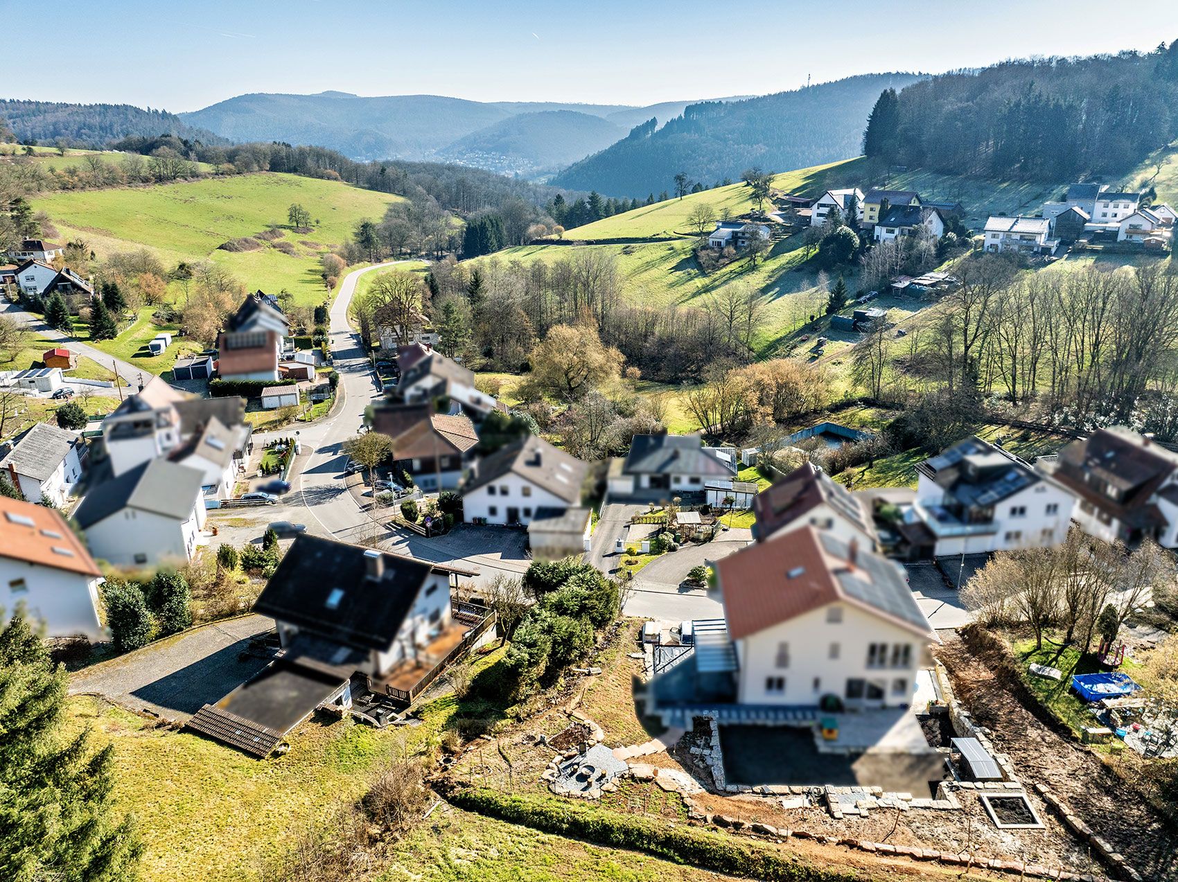 Luftaufnahme eines Wohngebiets mit mehreren Häusern und grünen Hügeln im Hintergrund.