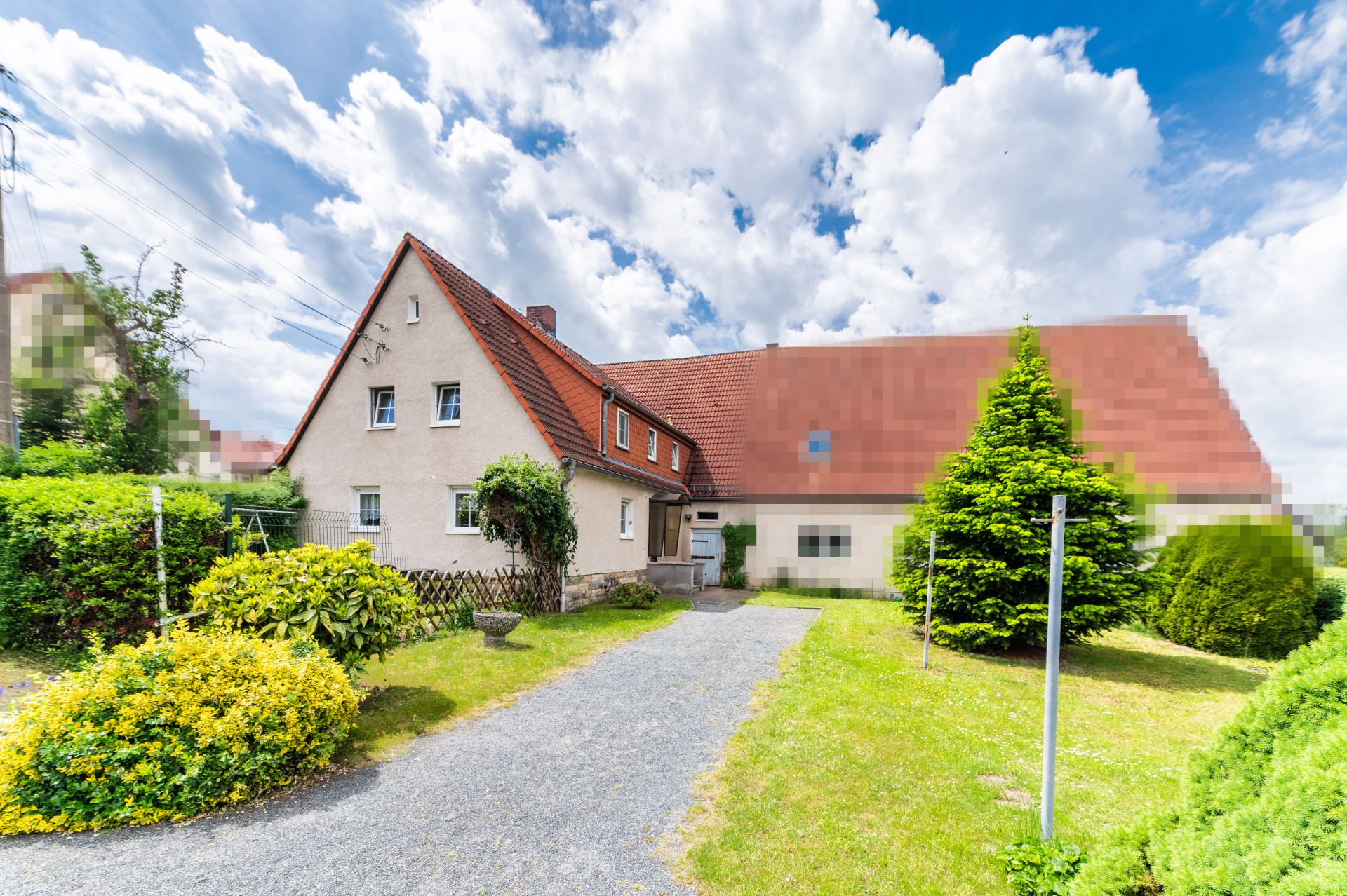 Gepflegtes Wohnhaus mit rotem Dach, Garten, Sträuchern und kleinem Weg im Vordergrund.