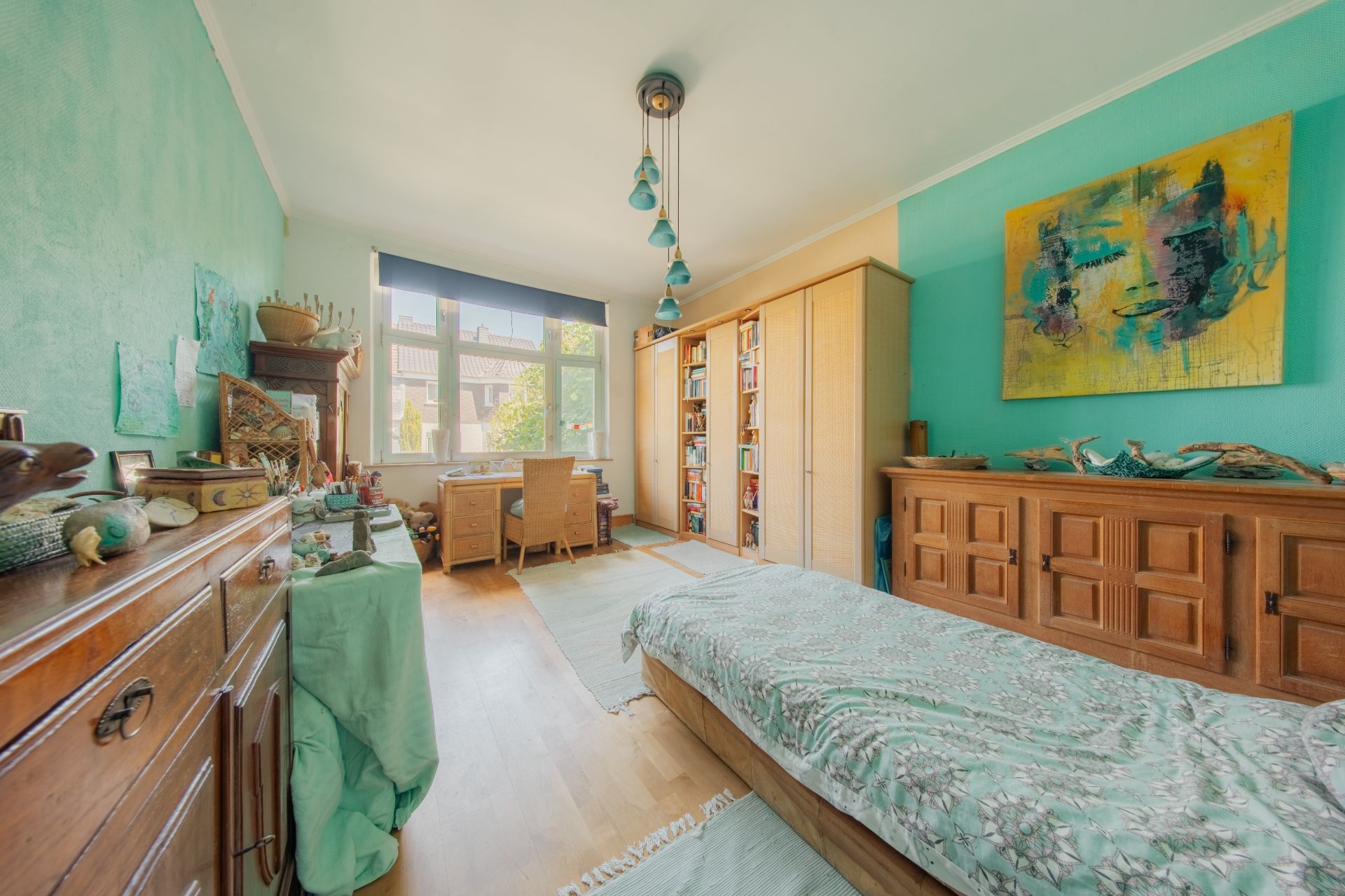 Helles Schlafzimmer mit Einzelbett, großem Fenster, Schreibtisch und Holzmöbeln.