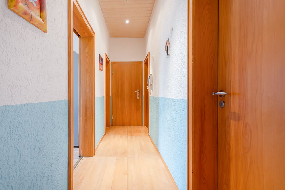 Heller Flur mit Holztüren, Holzdecke und hellblauen Wänden in einer Wohnung.