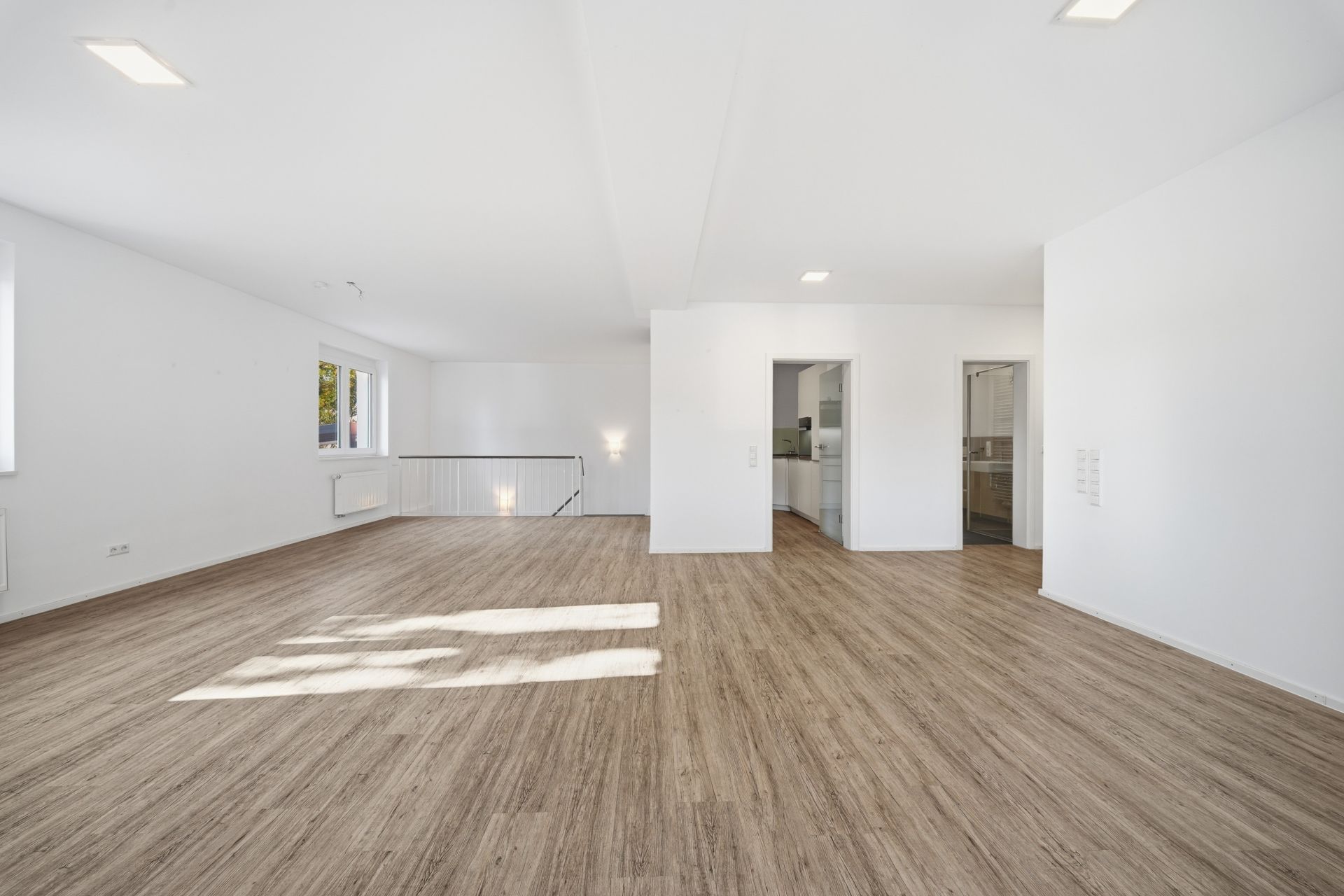 Heller Raum mit Holzfußboden, weißen Wänden und zwei Türen, Fenster auf der linken Seite.