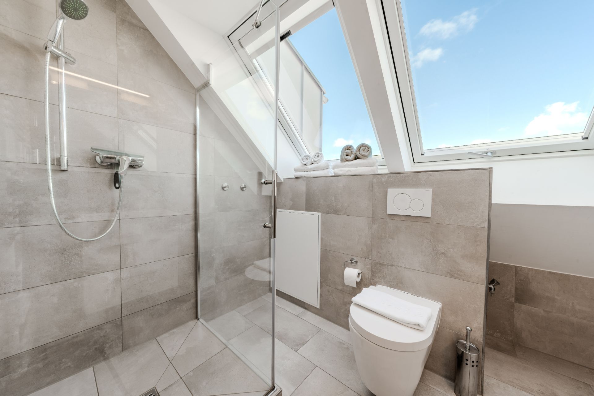 Modernes Badezimmer mit Dusche, Toilette, großen Fenstern und gefalteten Handtüchern auf der Fensterbank.