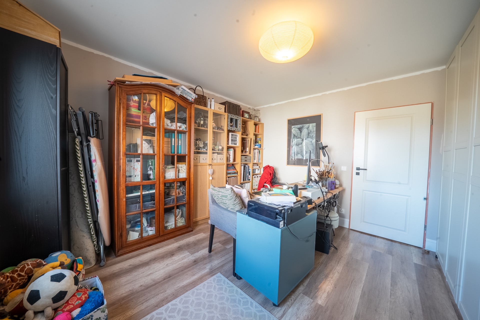 Helles Arbeitszimmer mit Regalen, Schreibtisch, Stühlen und Spielzeugkiste auf Holzfußboden.