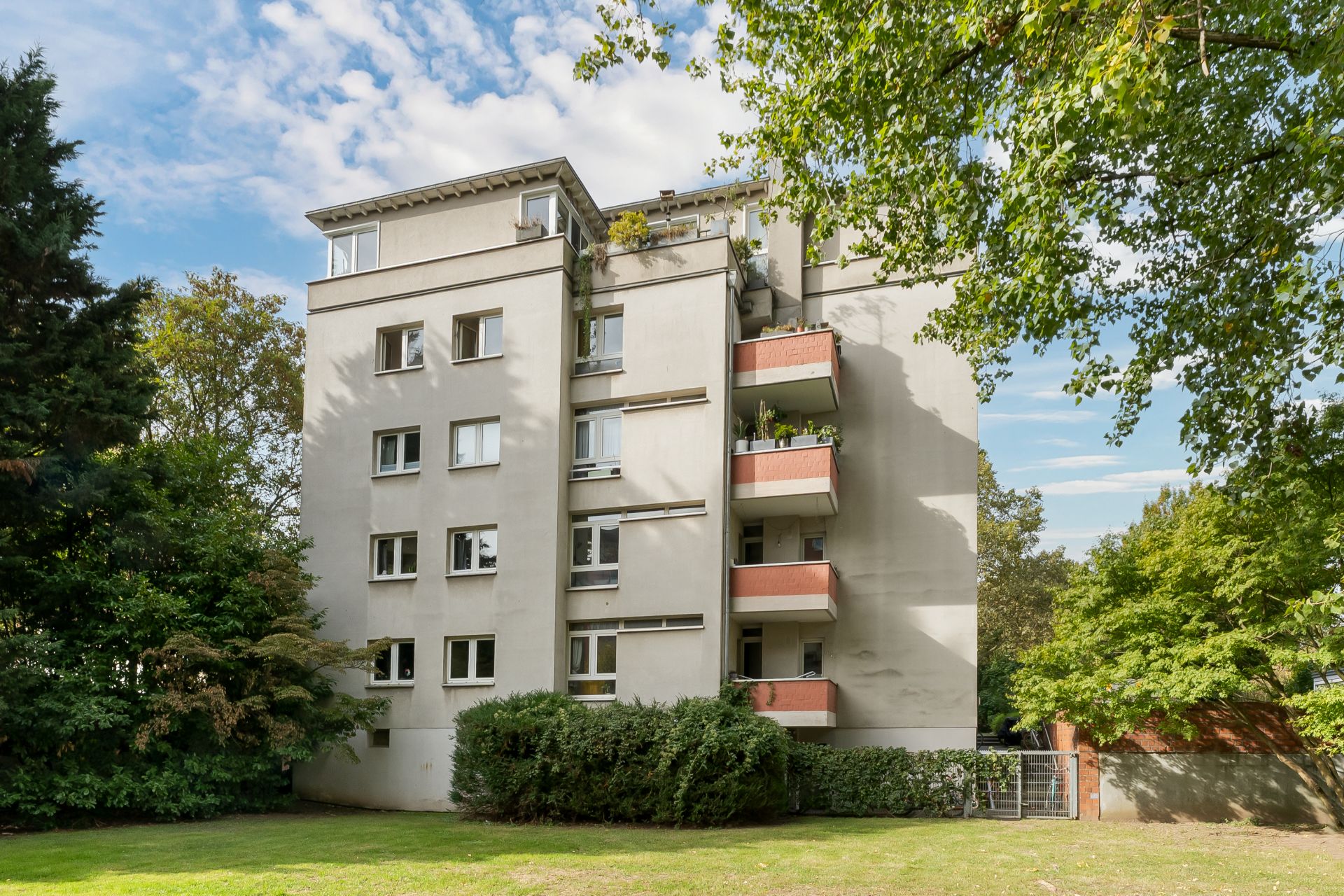 Mehrstöckiges Wohnhaus mit Balkonen, umgeben von Bäumen und Rasen.