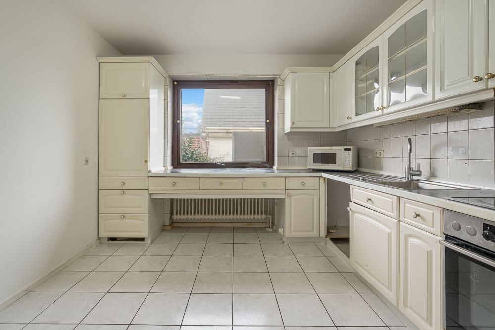 Helle Küche mit weißen Schränken, Fliesenboden, großem Fenster und eingebautem Herd.