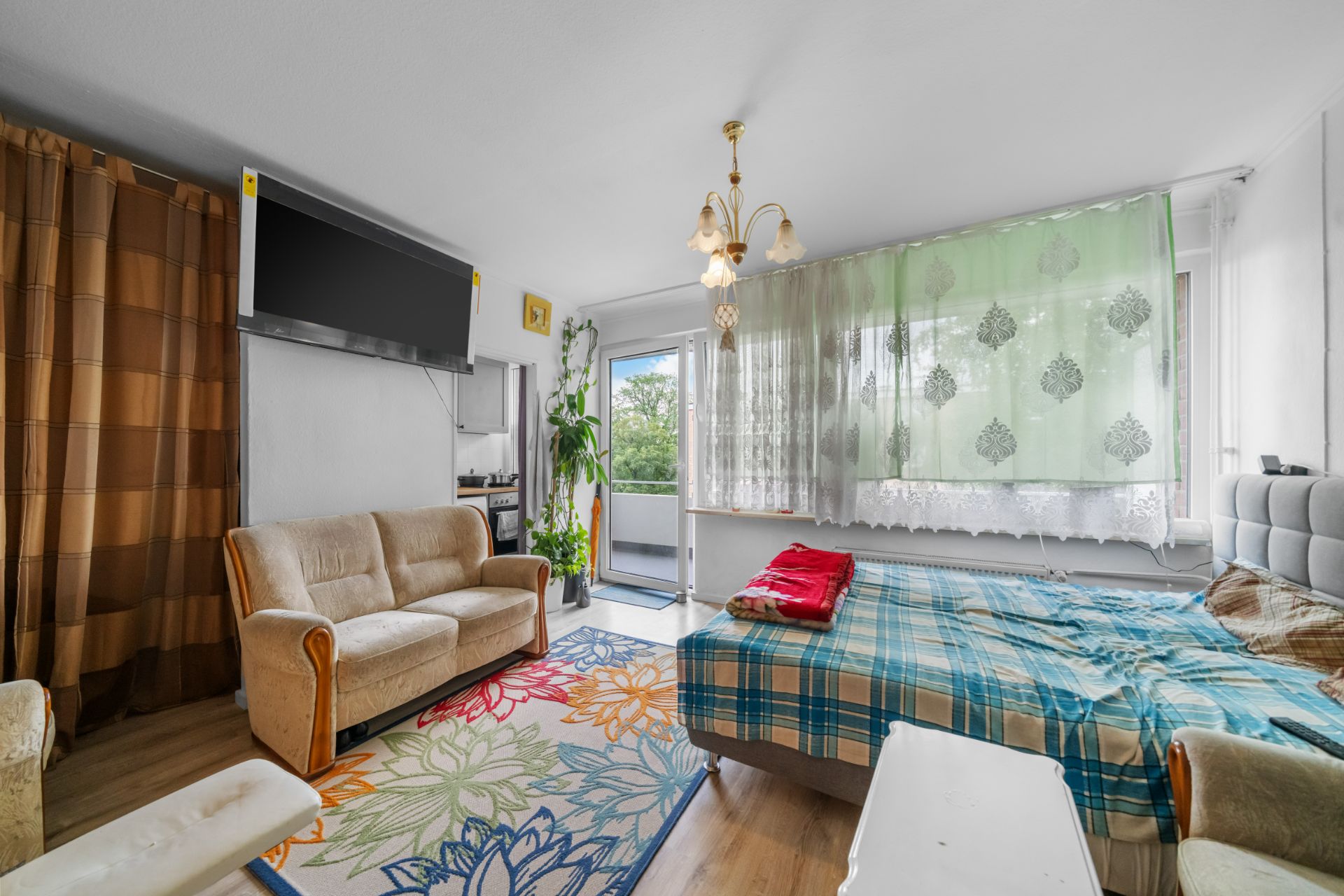 Helles Wohnzimmer mit Sofa, Bett, Teppich, Fernseher und Zugang zu einem Balkon.