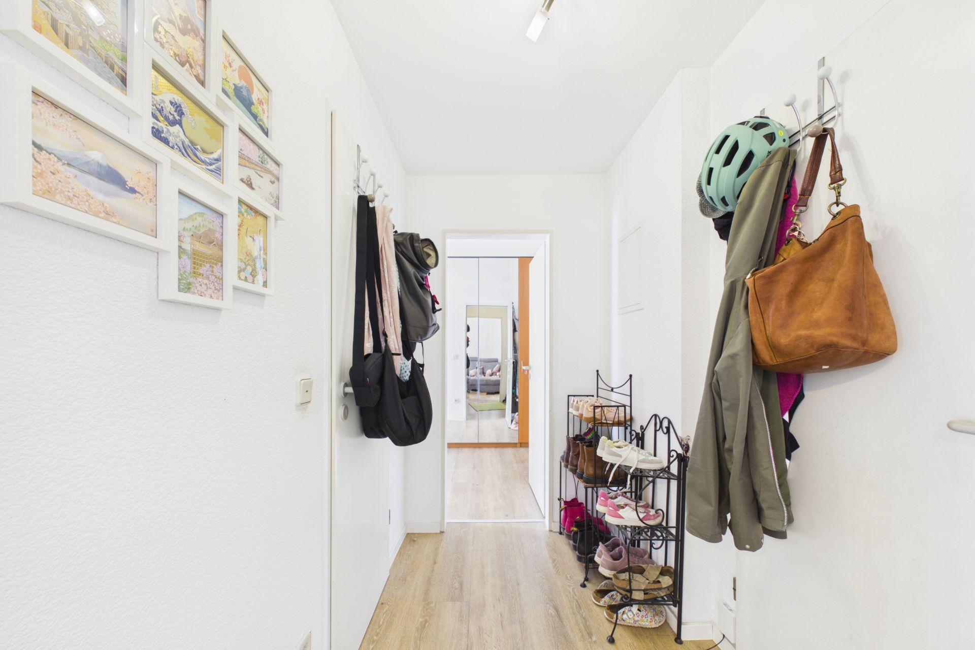 Heller Flur mit Garderobe, Schuhregal, Jacken, Taschen und Wandbildern in einer Wohnung.