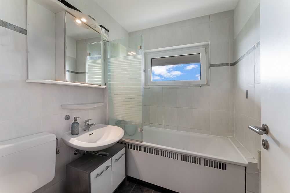Modernes Badezimmer mit weißer Badewanne, Waschbecken und Fenster.