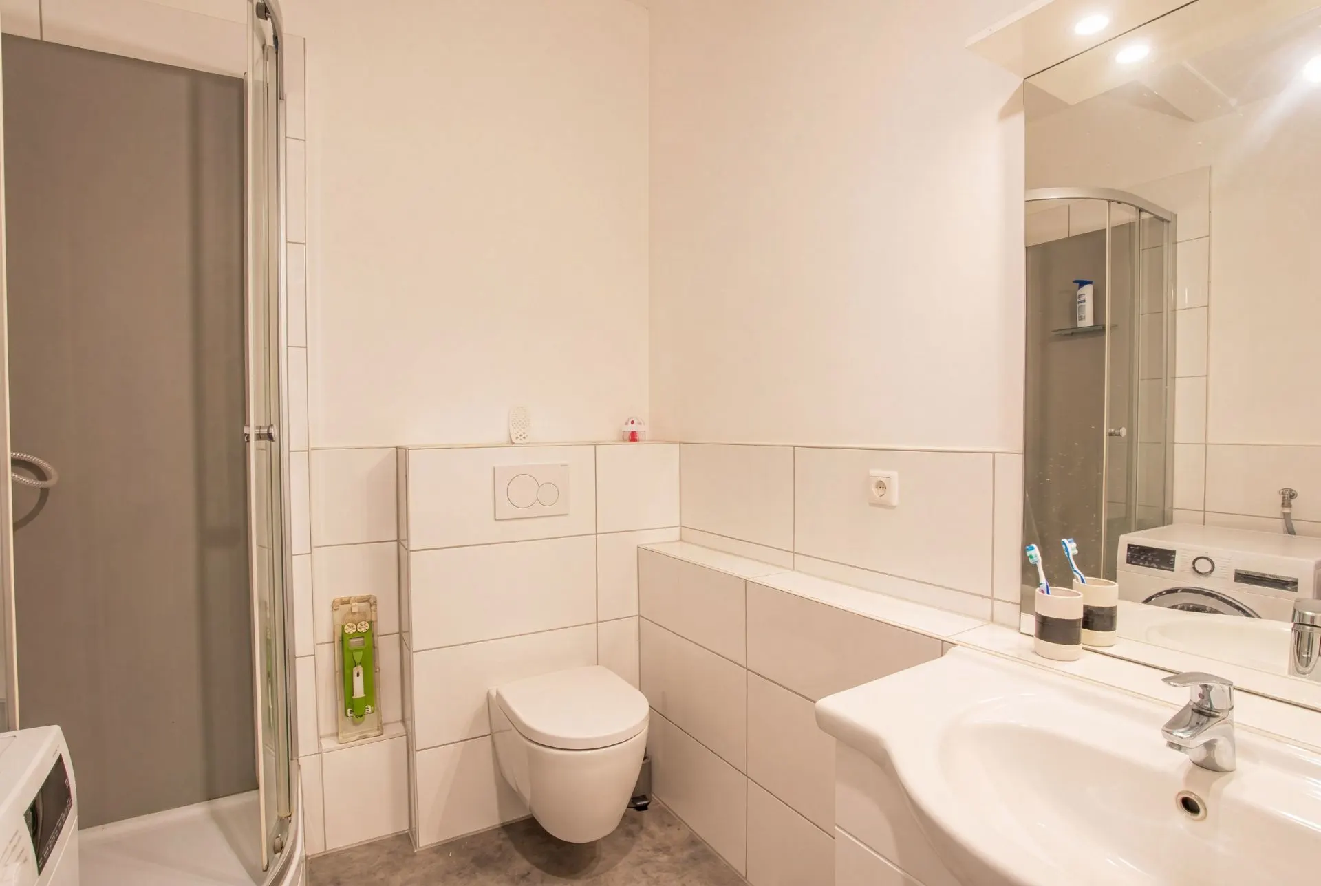 Modernes Badezimmer mit Dusche, WC, Waschbecken und großem Spiegel.