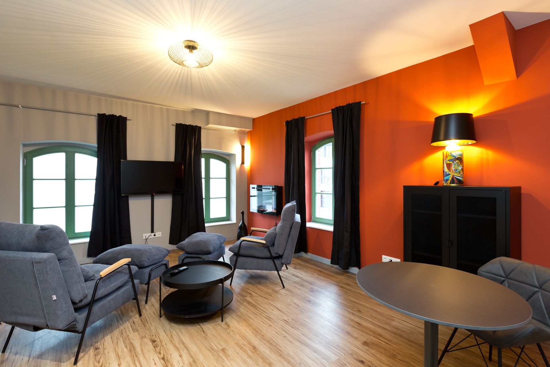 Helles Wohnzimmer mit orangefarbener Wand, grauen Sesseln, Tisch und Stehlampe.