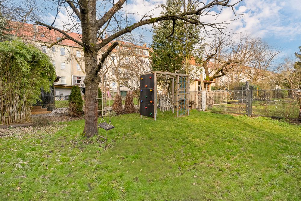 Grüner Garten mit Baum, Schaukel und Klettergerüst vor Wohnhäusern.