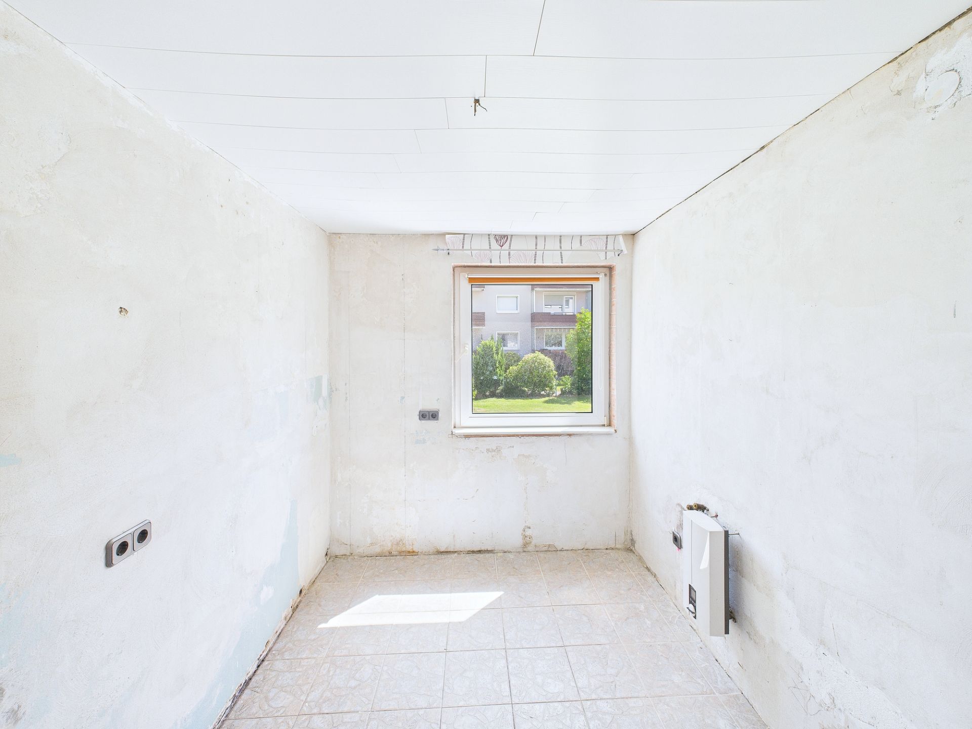 Leerer, renovierungsbedürftiger Raum mit einem Fenster und gefliesten Boden.