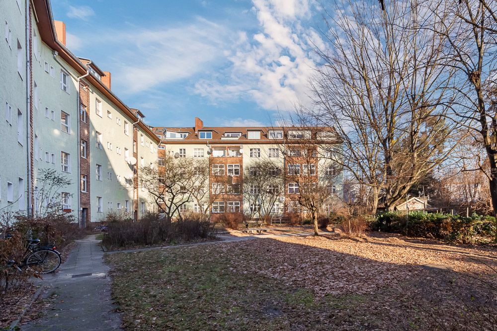 Wohnhäuser mit mehreren Stockwerken, Innenhof mit Bäumen und Gehweg, herbstliche Stimmung.