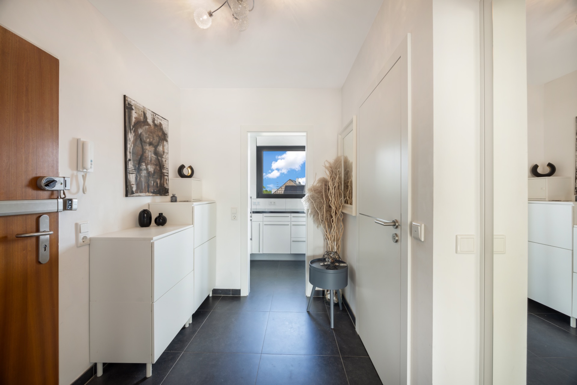 Heller Flur mit weißen Möbeln, Dekoration und Blick in eine Küche mit Fenster.