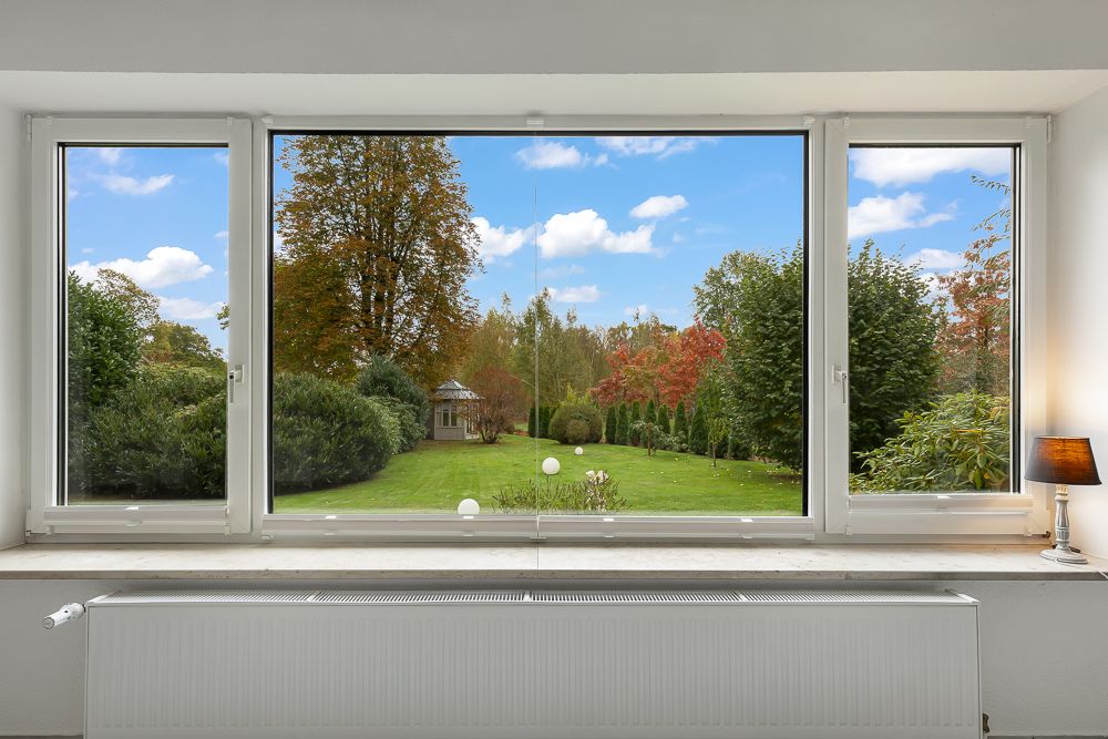 Großes Fenster mit Blick auf einen grünen Garten mit Bäumen und Rasen.