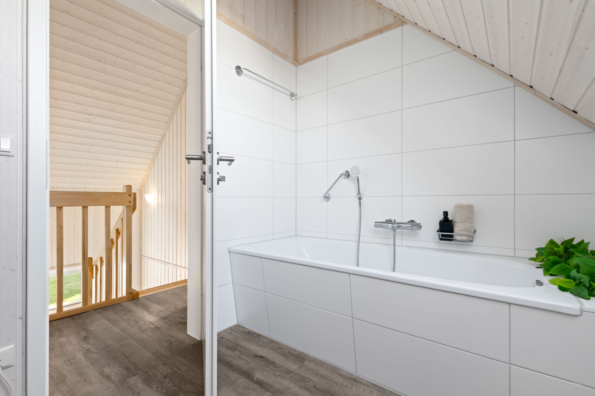 Modernes Badezimmer mit Badewanne, weißen Fliesen und Holzdecke unter Dachschräge.