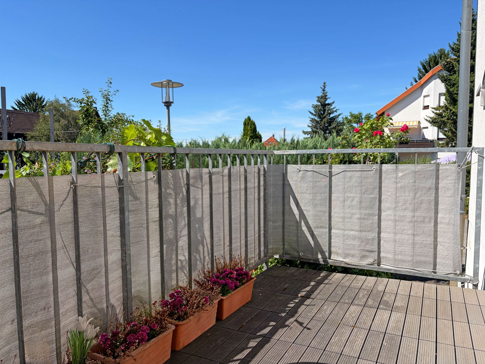 Balkon mit Blumenkästen, Holzfußboden und Sichtschutz, umgeben von Nachbarsgärten.