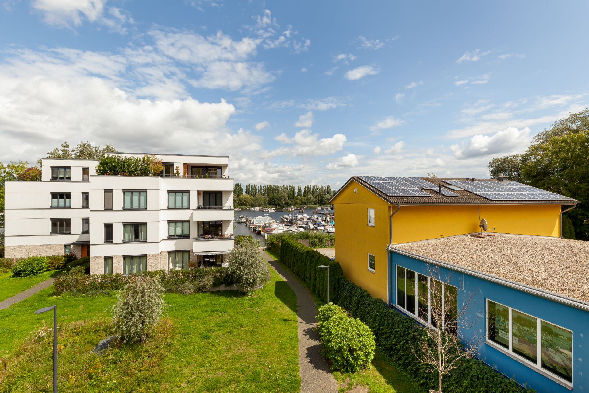Moderne Wohngebäude mit Garten und Fußweg, sonniger Himmel mit einigen Wolken.