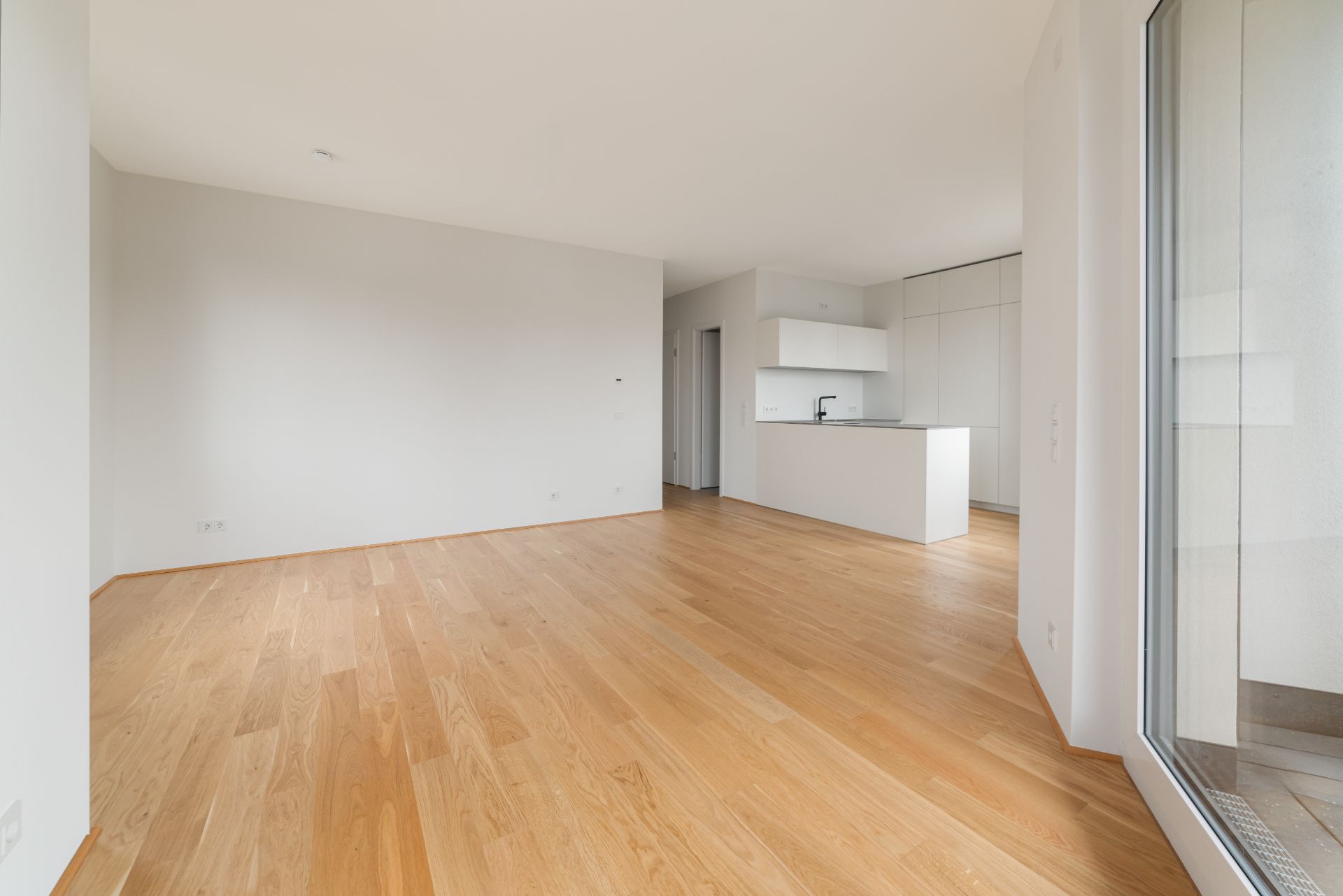 Heller Raum mit Holzfußboden, offener Küche und großer Fensterfront.