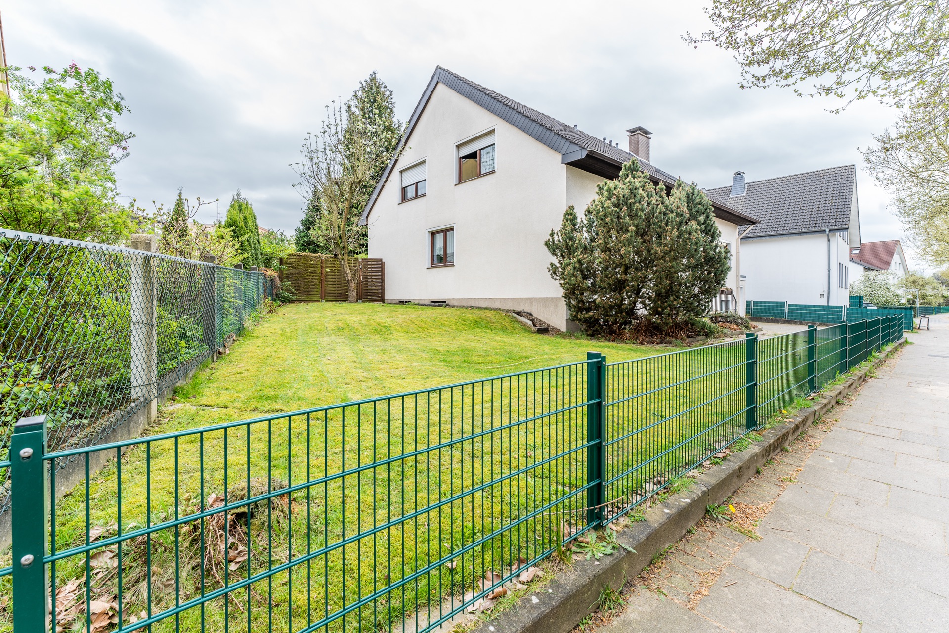 Ein weißes Wohnhaus mit Garten und grünem Zaun an einer Gehwegstraße.