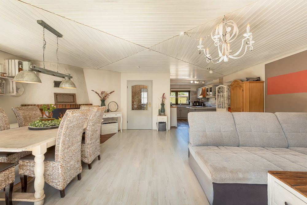 Wohnzimmer mit grauem Sofa, Esstisch mit Korbstühlen und Kronleuchter an der Decke.