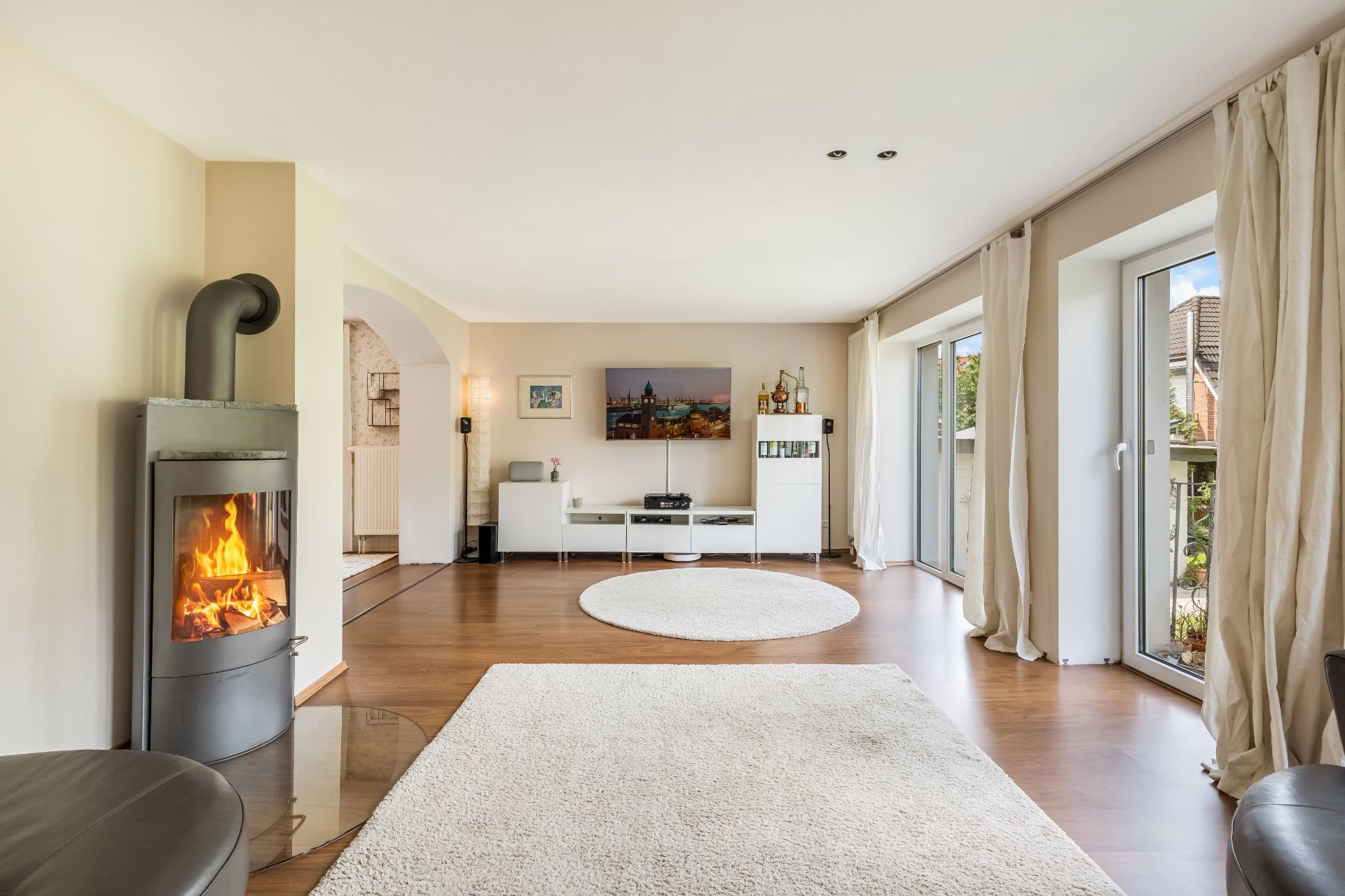 Helles Wohnzimmer mit Kamin, großen Fenstern, Teppichen und modernen Möbeln.