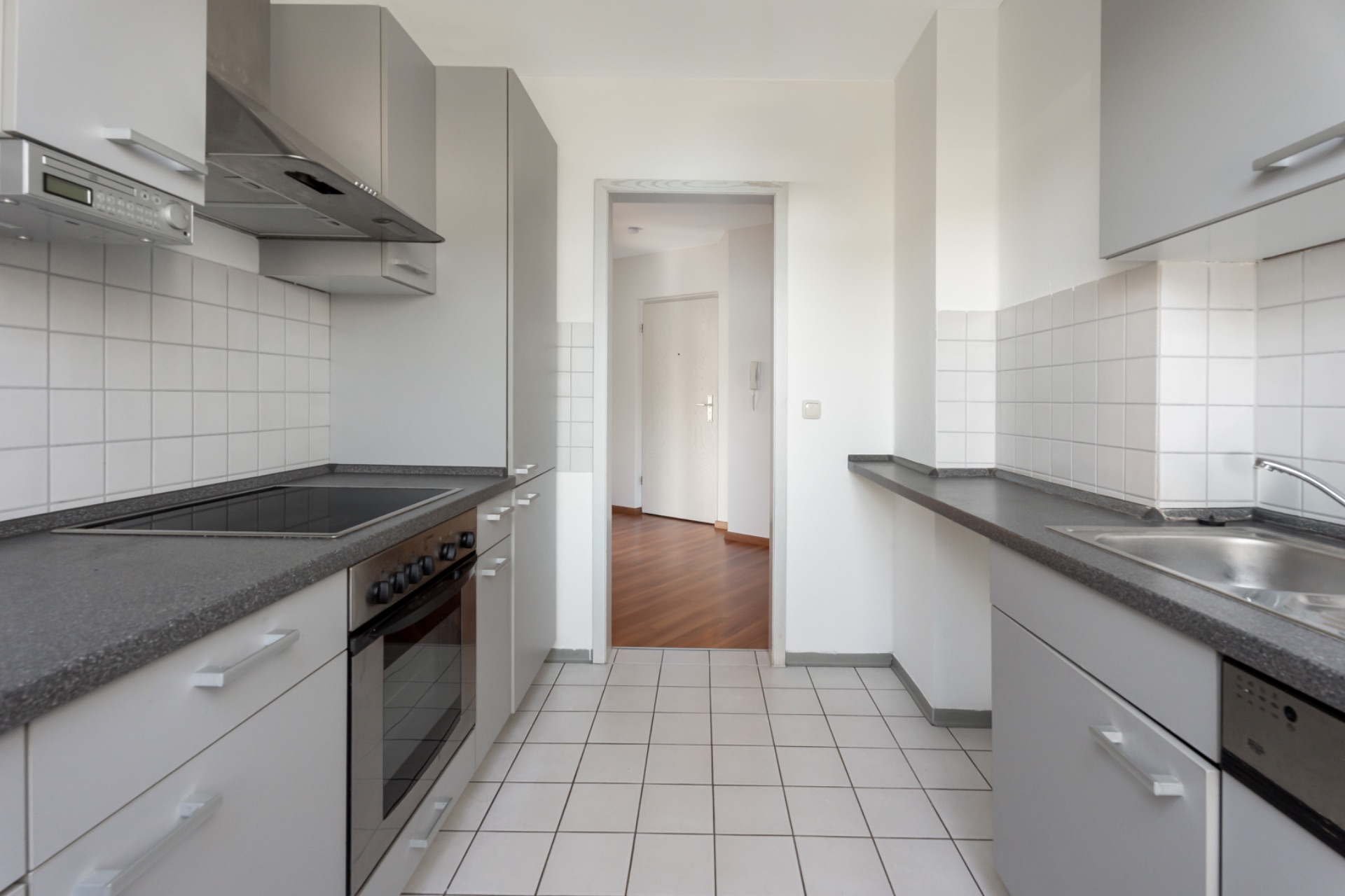 Moderne, helle Küche mit grauen Schränken, Herd, Ofen und Spüle, Blick in den Flur.