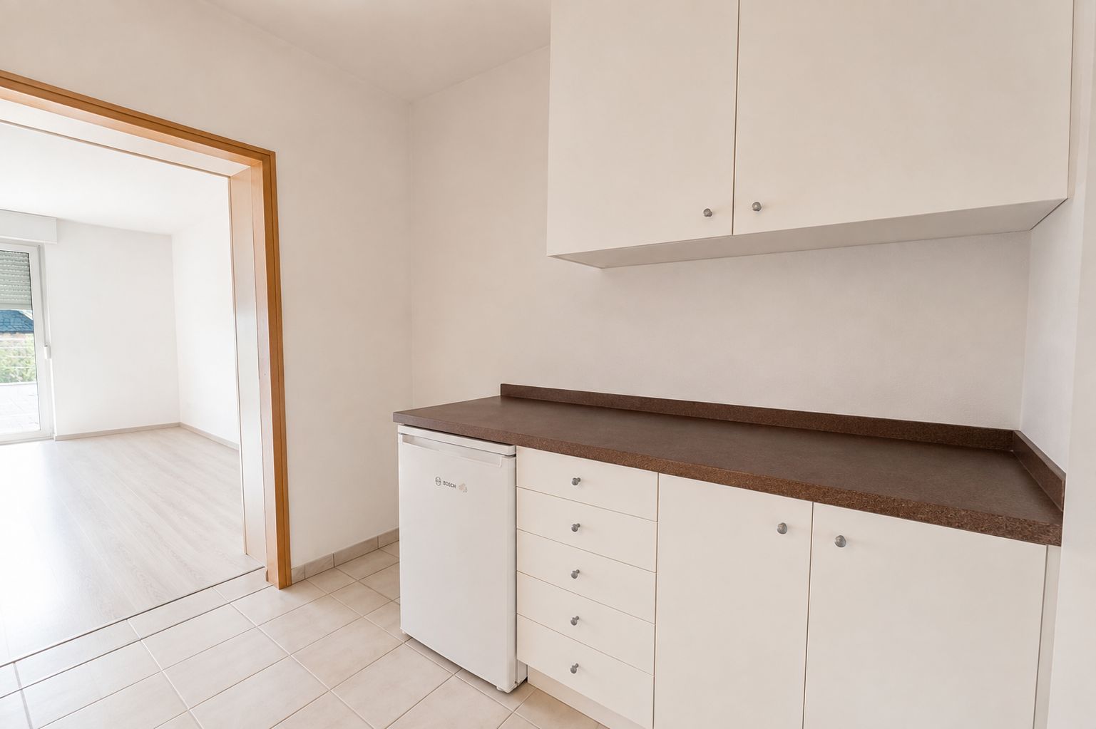 Kleine Küche mit brauner Arbeitsplatte, weißen Schränken und kleinem Kühlschrank.