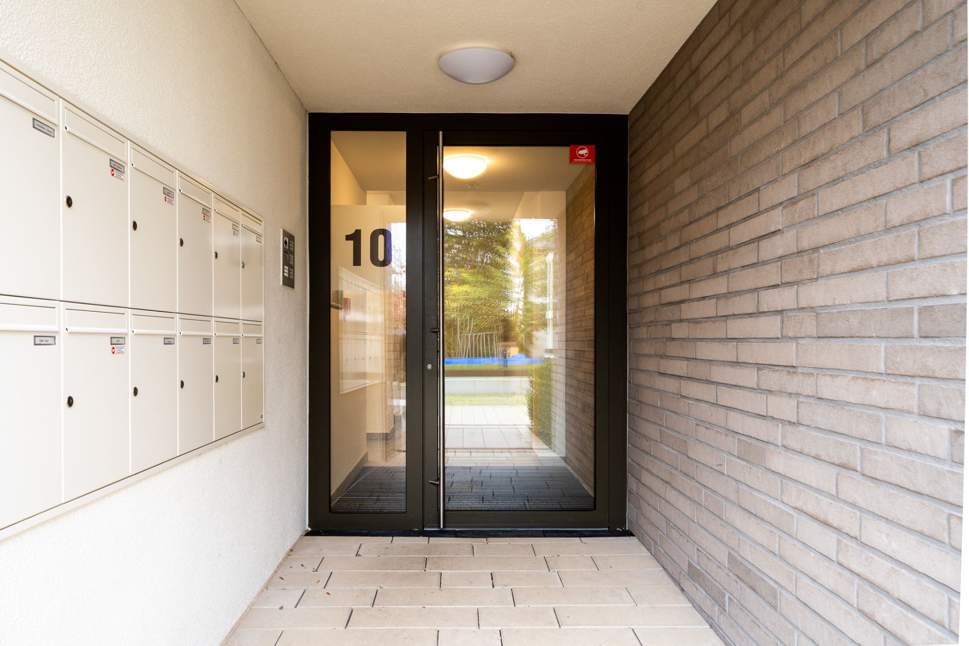 Eingangsbereich mit Glastür, Hausnummer 10 und Briefkästen an der Wand.