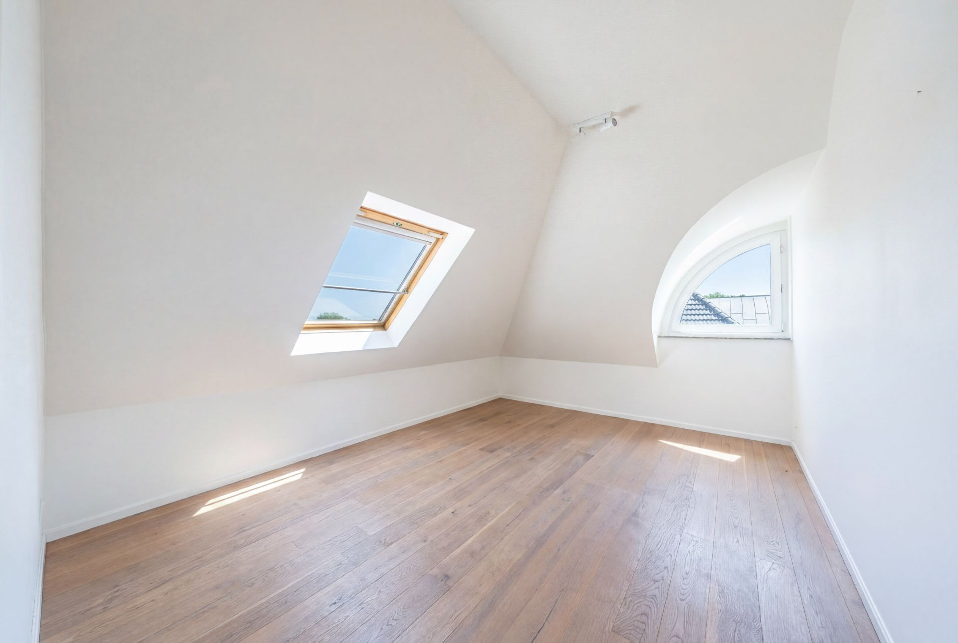 Leerer Dachraum mit Holzfußboden und zwei Fenstern in schrägen Wänden.