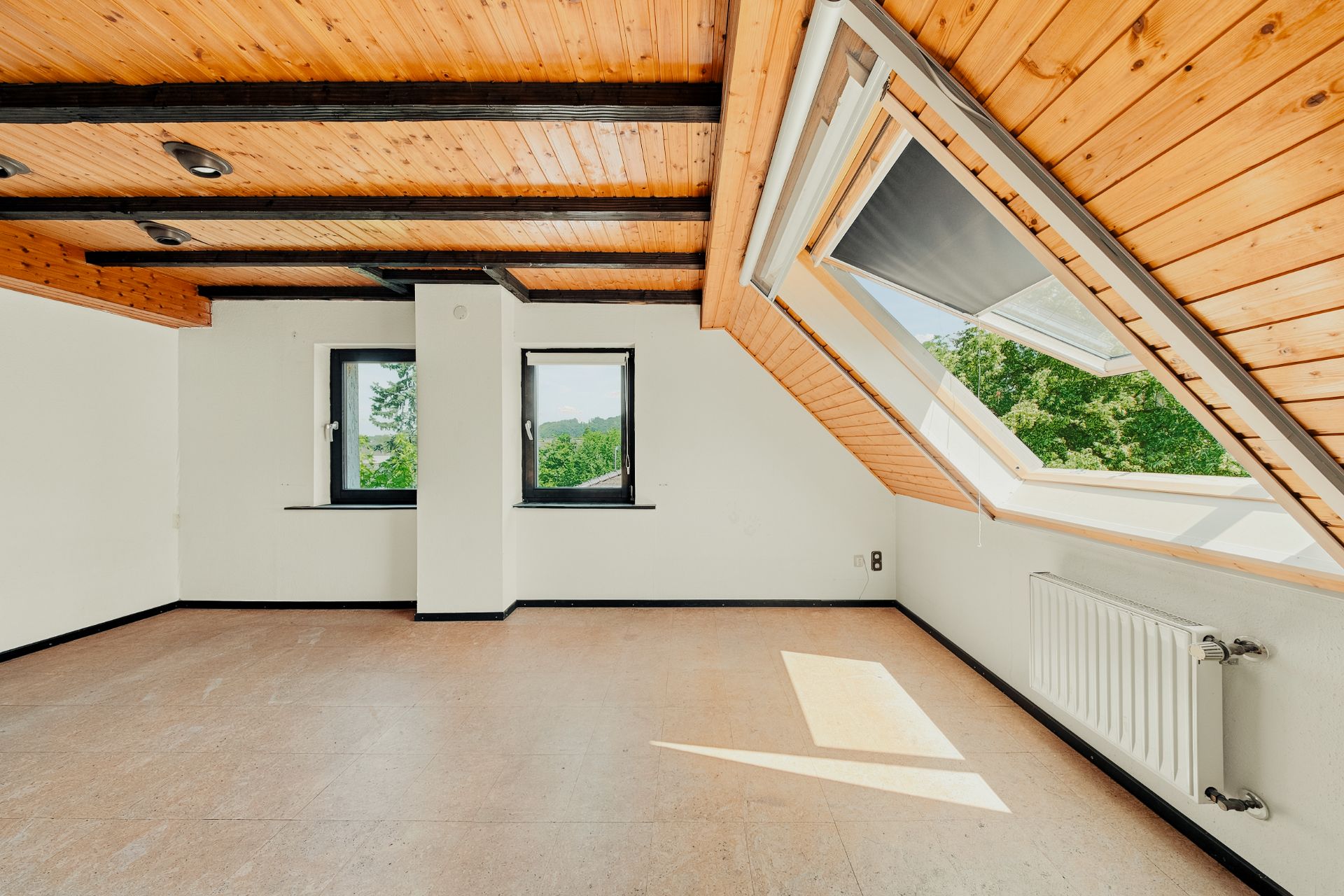 Heller Dachraum mit Holzdecke, zwei Fenstern und großem Dachfenster, Heizkörper an der Wand.
