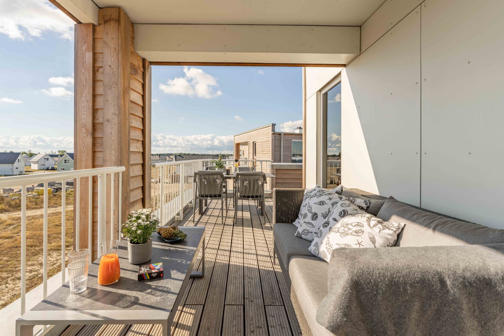 Überdachter Balkon mit Sofa, Tisch und Stühlen, Blick auf Wohnhäuser im Freien.
