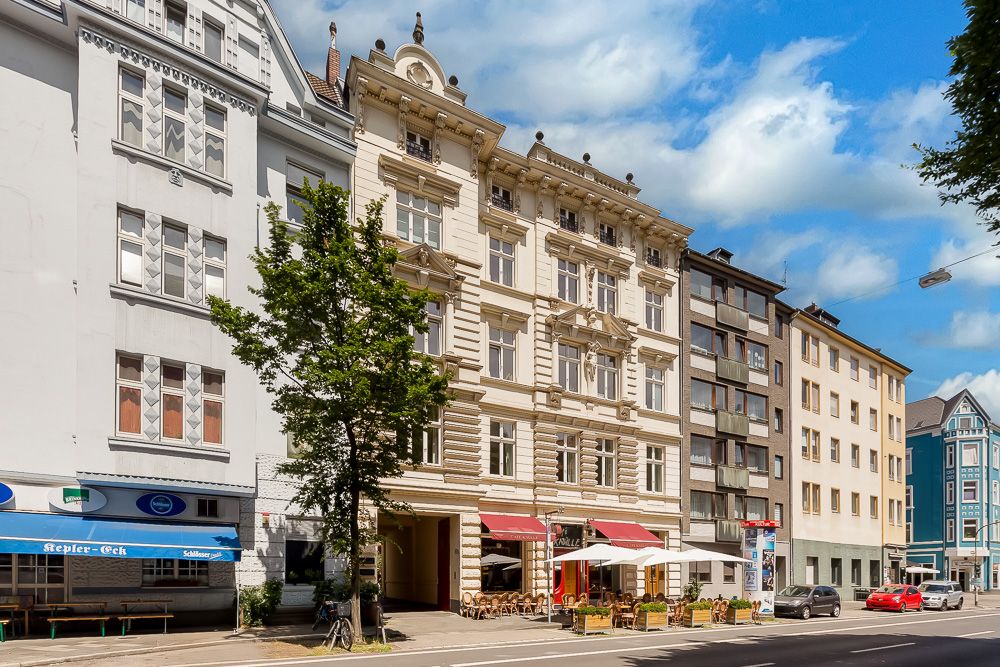 Historisches Wohngebäude mit Cafétischen auf dem Bürgersteig und Bäumen an der Straße.