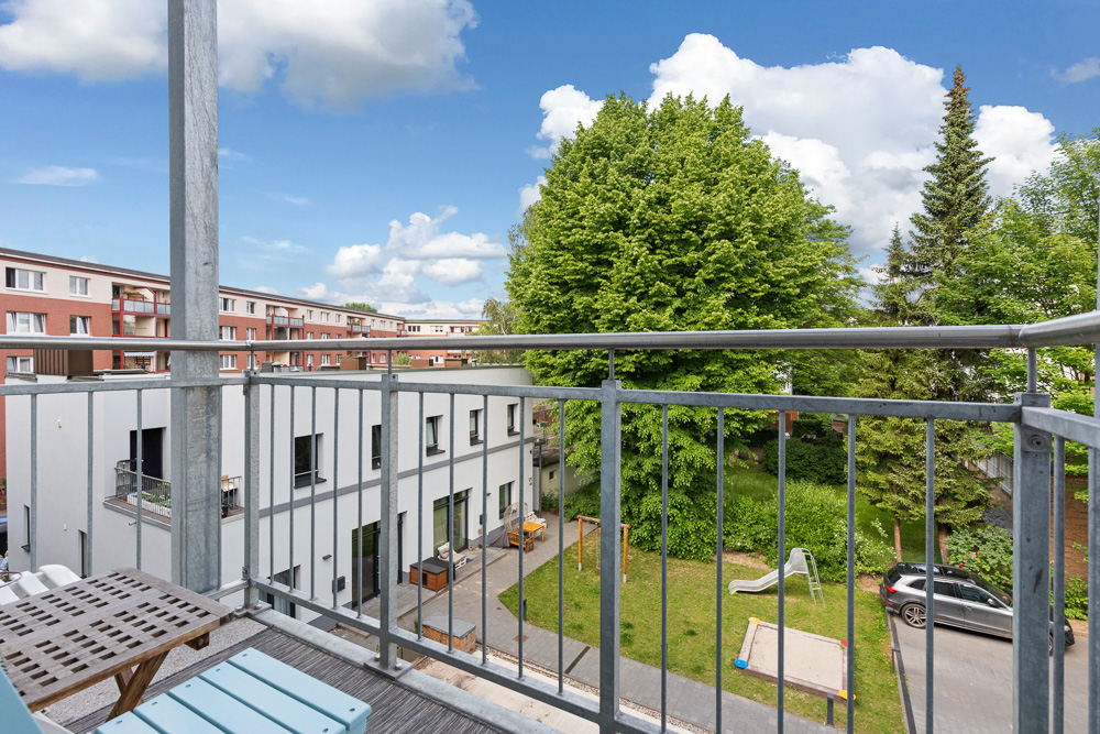 Blick von einem Balkon auf einen grünen Innenhof mit Spielplatz, Sandkasten und Bäumen.